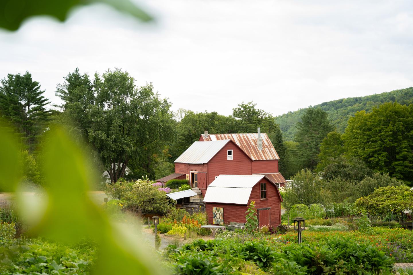 Red farmhouse surrounded by lush greenery on a cloudy day.