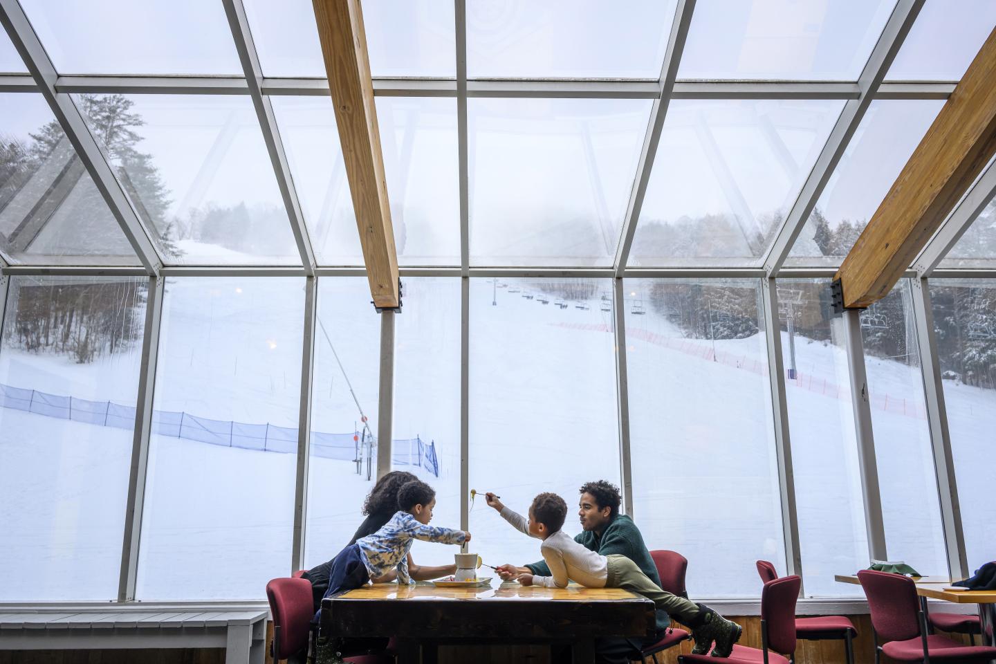Family dining in a cafe with large windows overlooking a snowy ski slope.