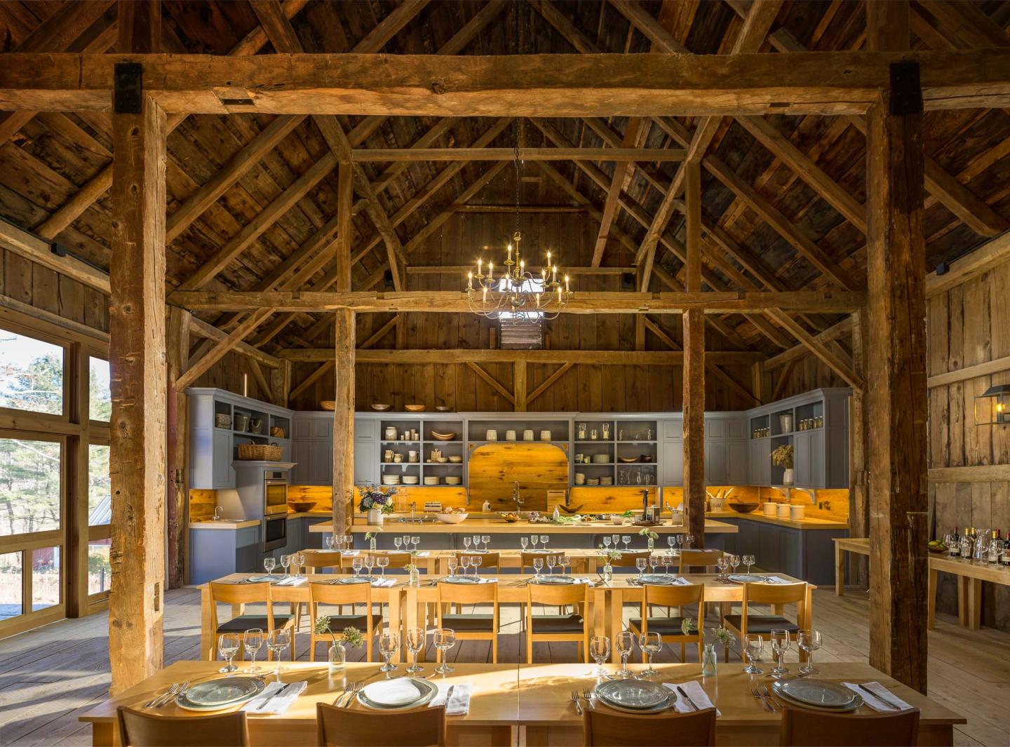 Rustic dining room with wooden beams, set tables, and open kitchen.