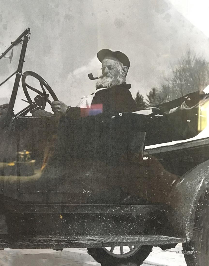Black and white photo of a man with a pipe driving an old car.