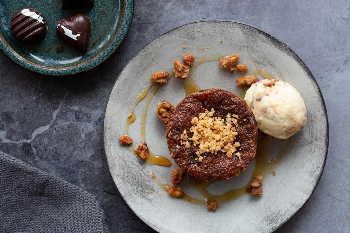 Sticky toffee pudding with ice cream on a plate, chocolates nearby.