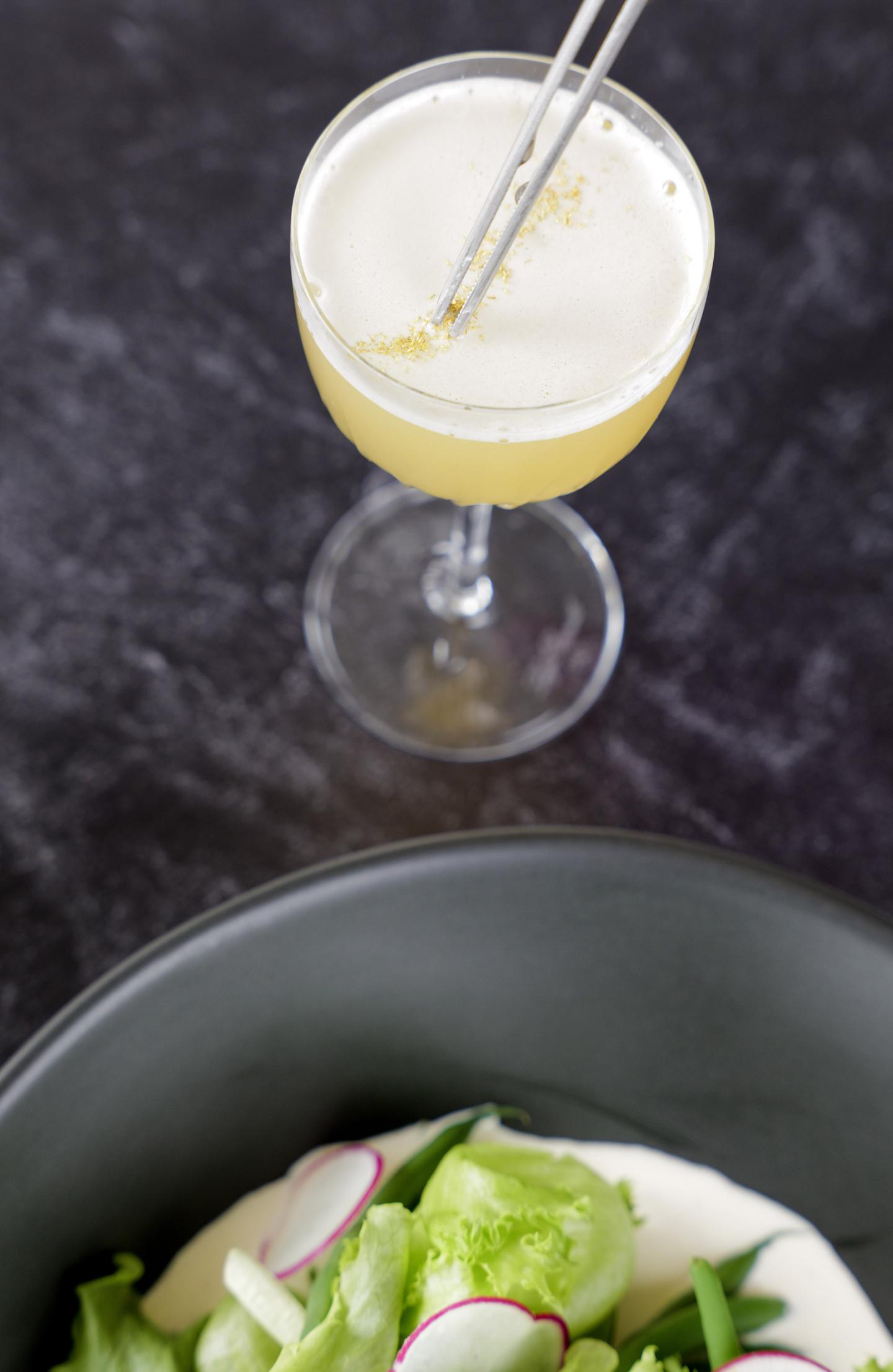 Cocktail with a slice and salad bowl on dark table.