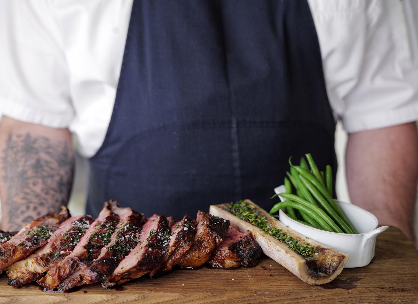 Sliced steak with green beans and bone marrow on a wooden board.