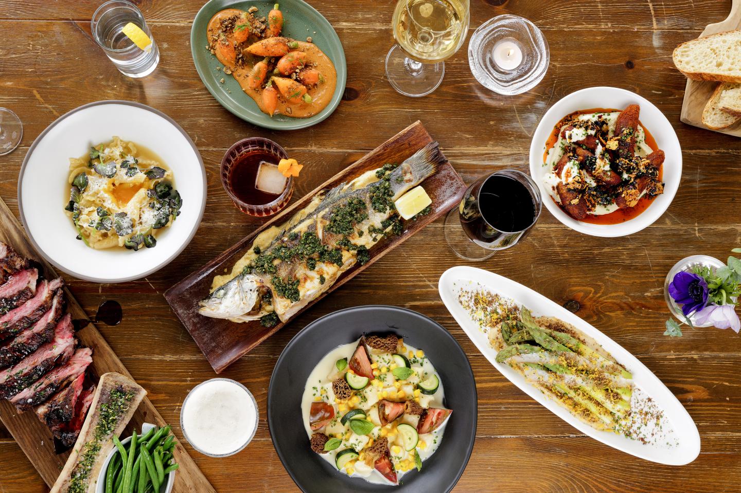 A variety of gourmet dishes on a wooden table with drinks.