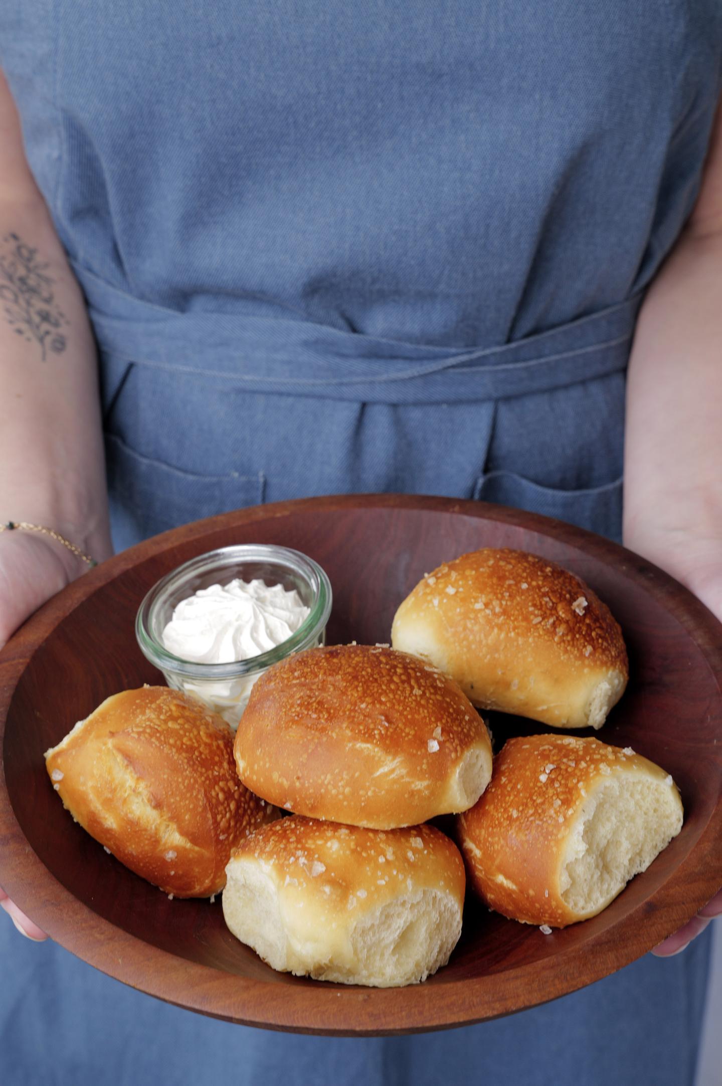 A person holds a plate of bread rolls with a small dish of butter.