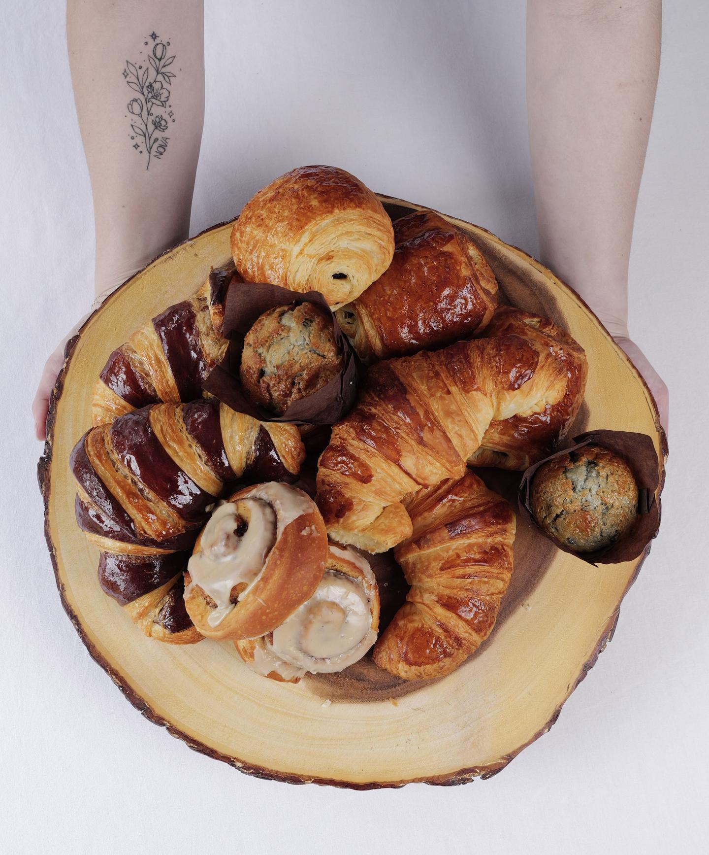 Assorted pastries on a wooden platter held by arms with a tattoo.