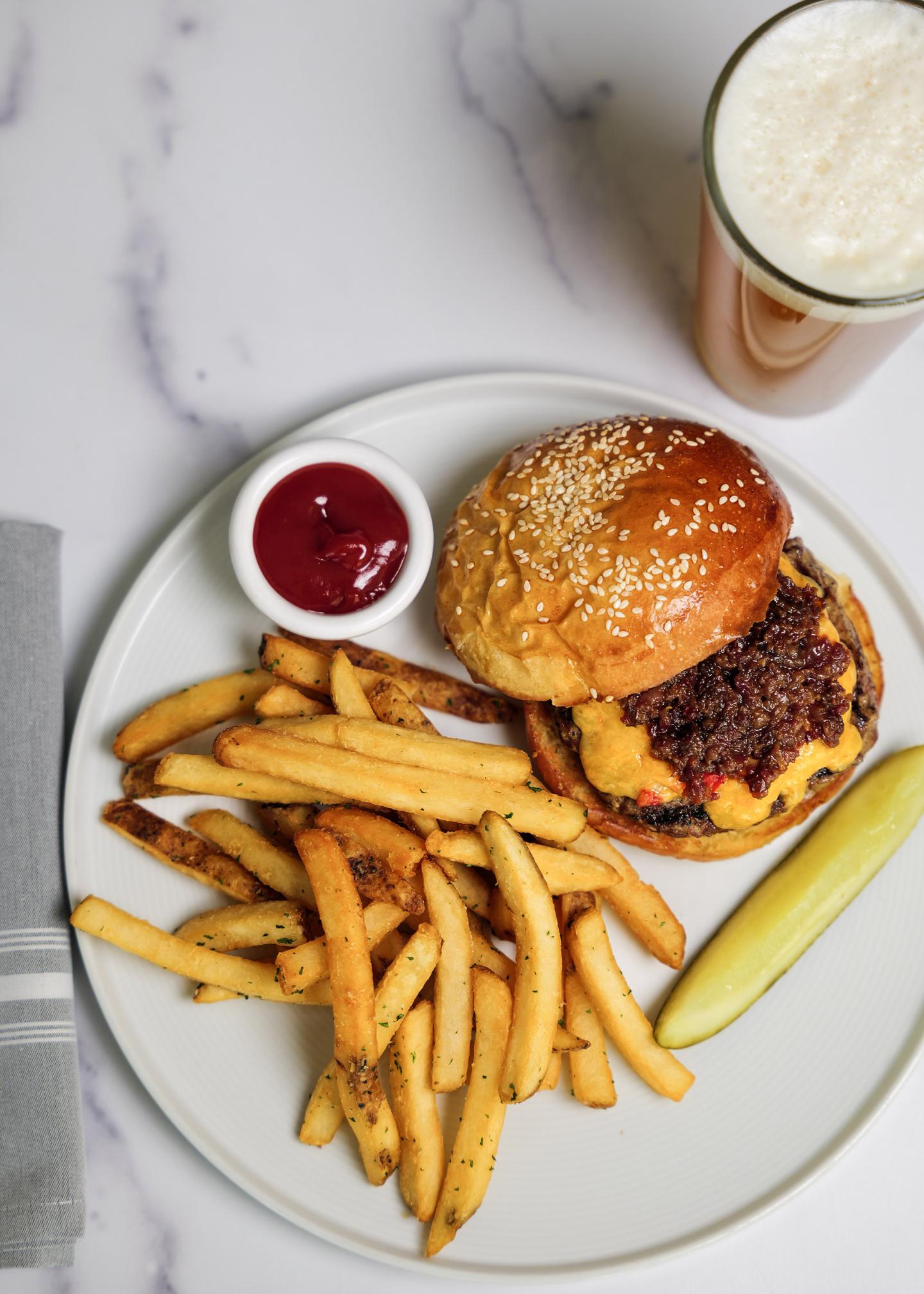 Burger with fries, a pickle, and ketchup on a plate, with a glass of beer.