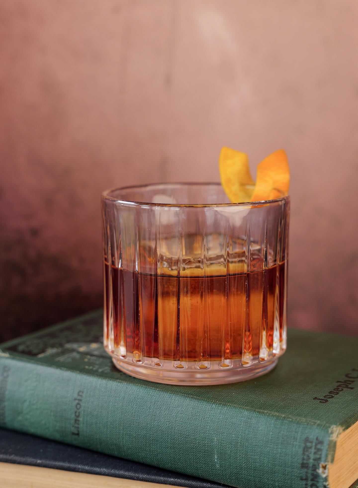 Whiskey glass with orange peel on stacked books.