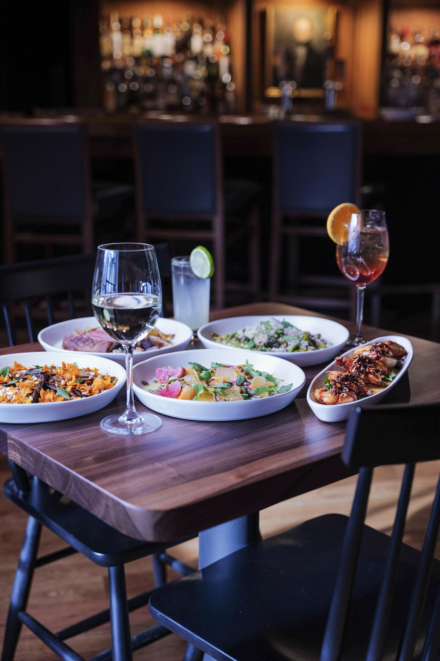 Plates of food and drinks on a wooden table in a dimly lit restaurant.