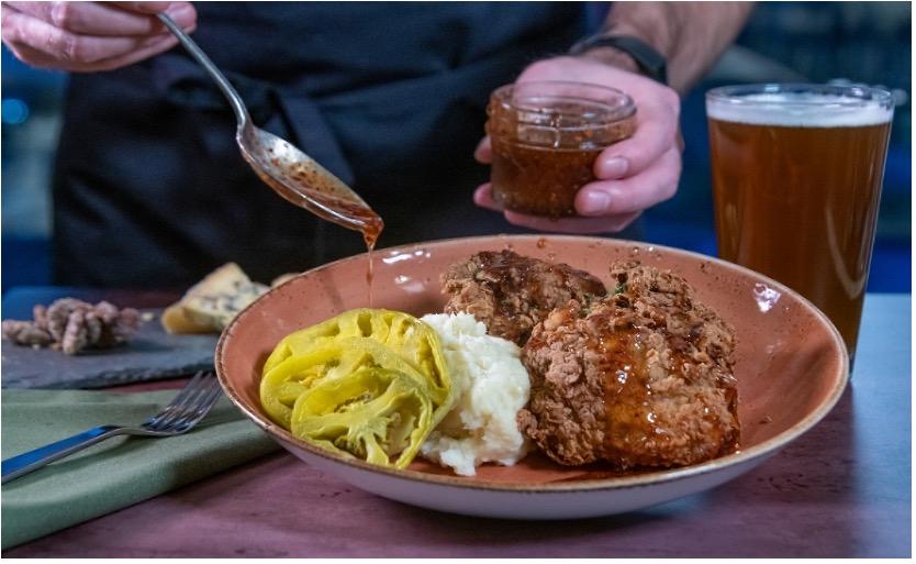 Fried chicken, mashed potatoes, and pickles on a plate with sauce being added.