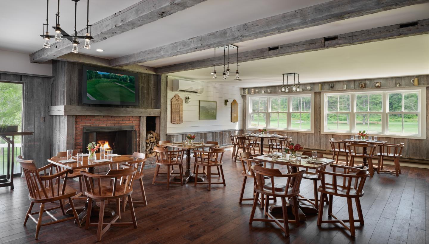 Spacious dining room with wooden tables and large windows, overlooking greenery.