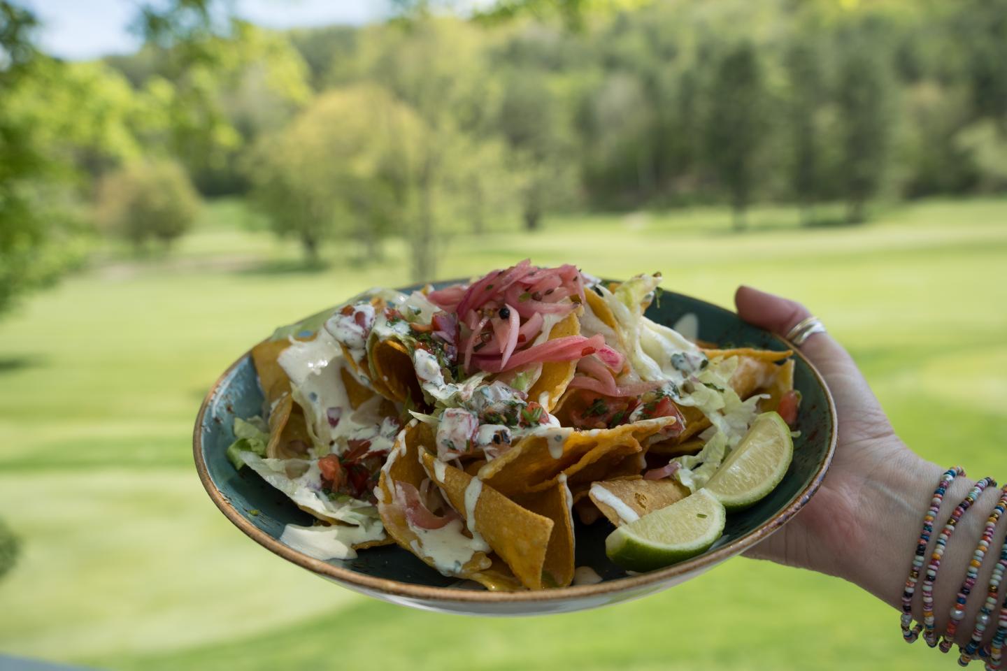 Nachos with toppings on a plate, held in a grassy outdoor setting.