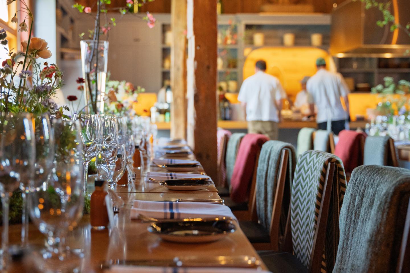 Restaurant table set with glasses; chefs working in the background.