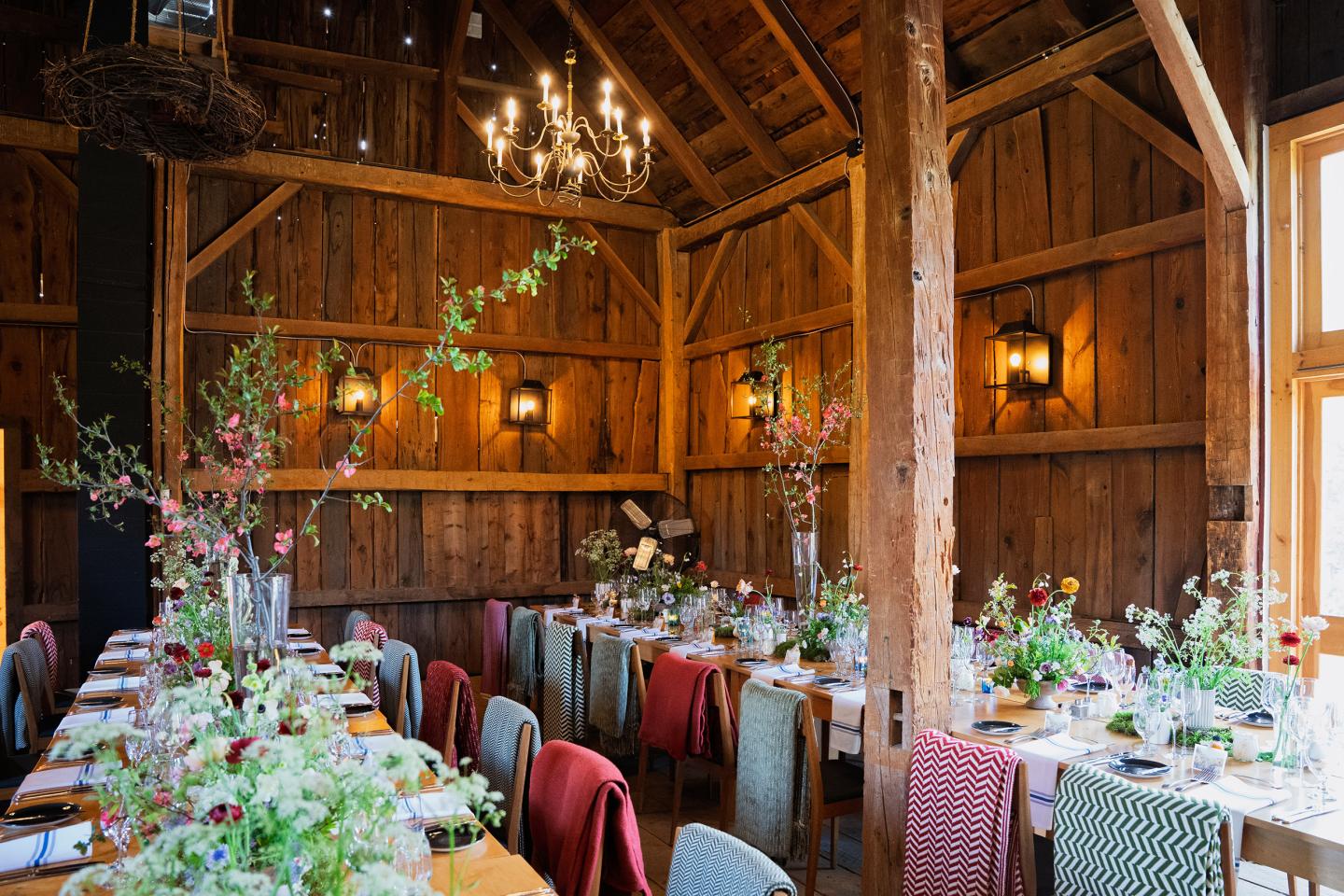 Rustic dining room with wooden walls, chandeliers, and floral centerpieces.
