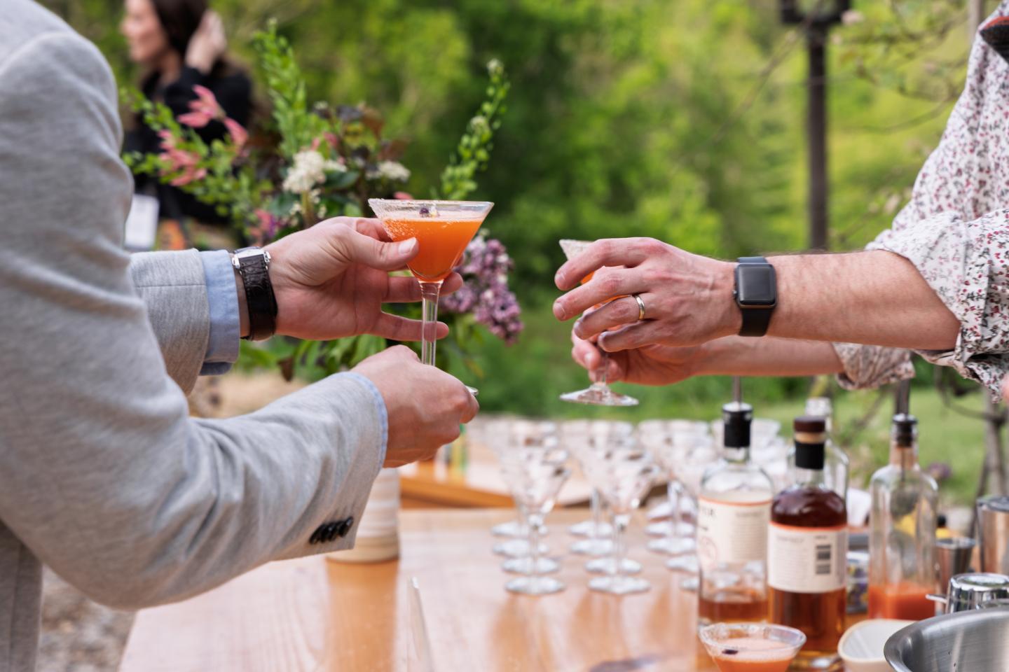 Two people exchange cocktails at an outdoor bar setting.