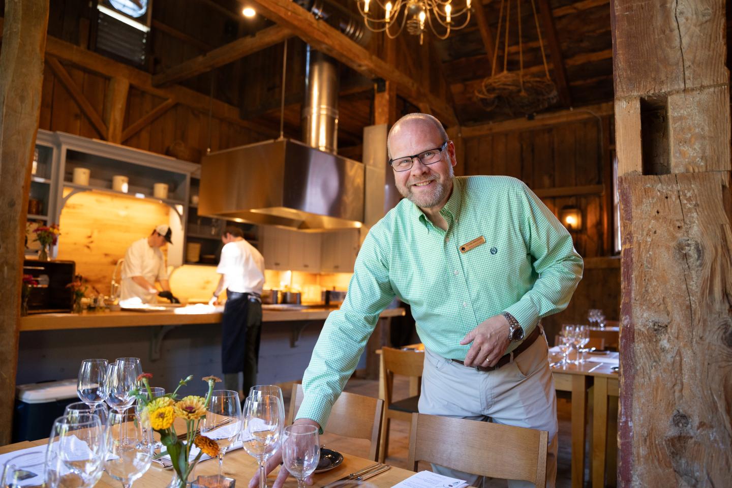 Restaurant staff arranging table in cozy, rustic setting with chefs in the background.