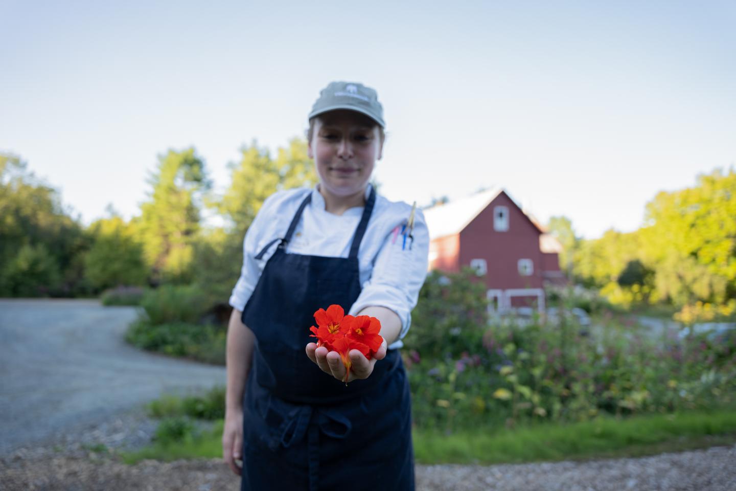 Chef holding red flower in front of a red barn.