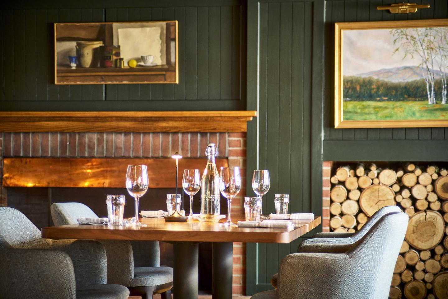 A cozy restaurant table set with wine glasses and a lit fireplace in the background.