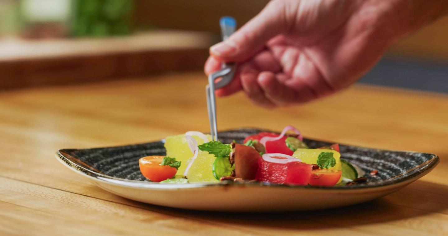 Hand placing garnish on a colorful salad on a ceramic plate.
