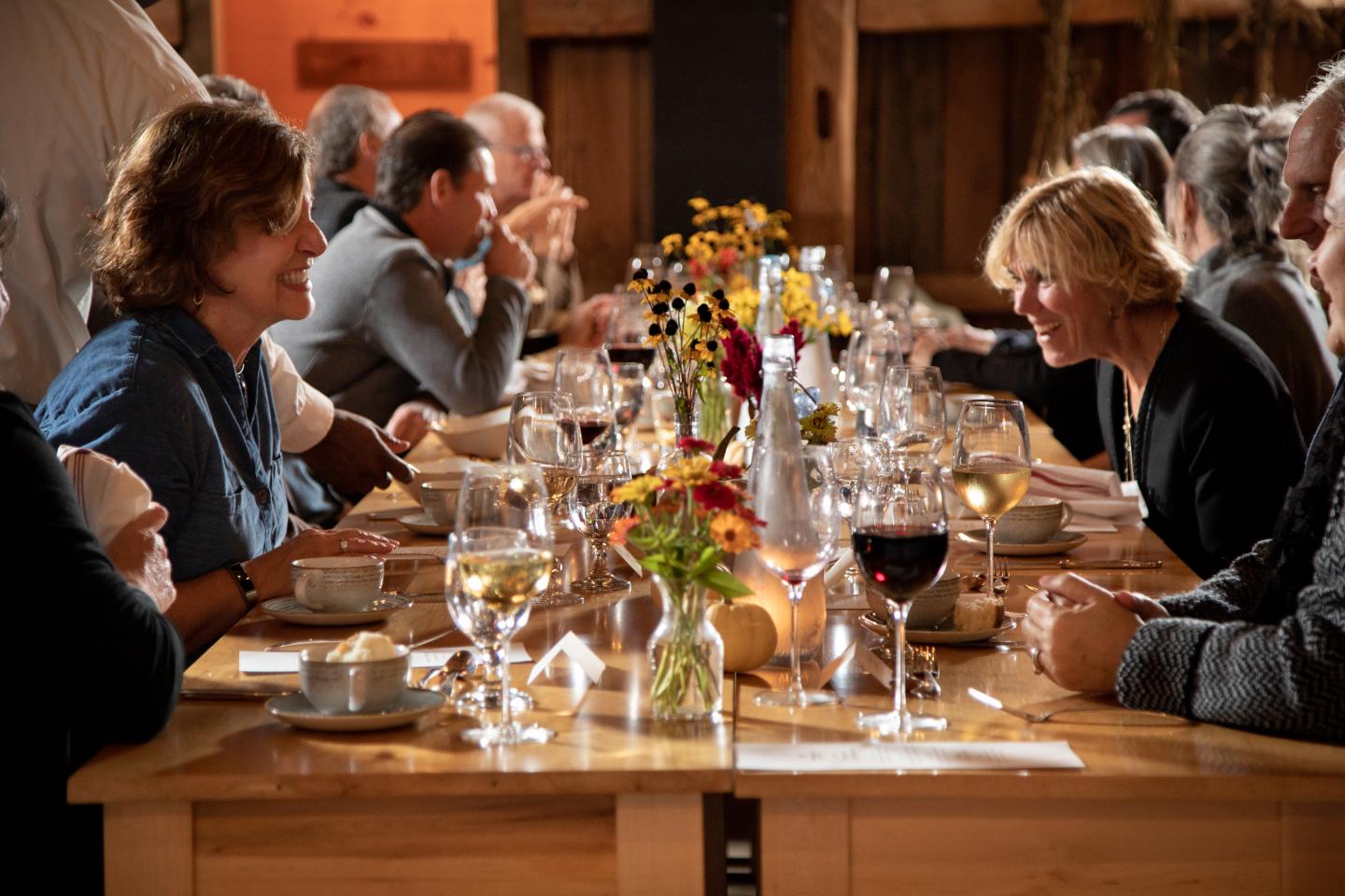 Cozy dinner party with guests chatting at a long table, adorned with flowers and wine glasses.