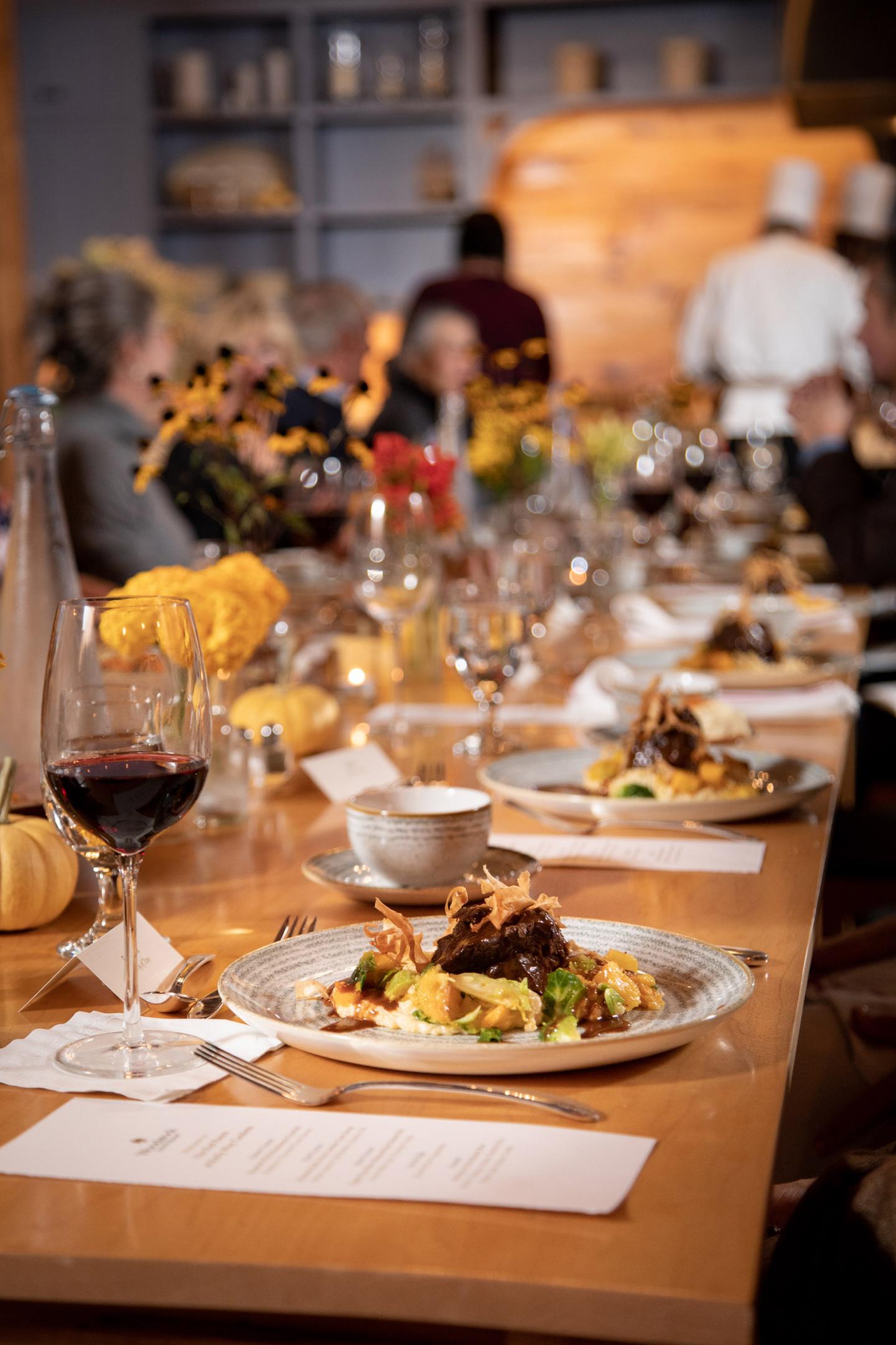 Elegant dining table with plated meals and wine glasses, people in the background.