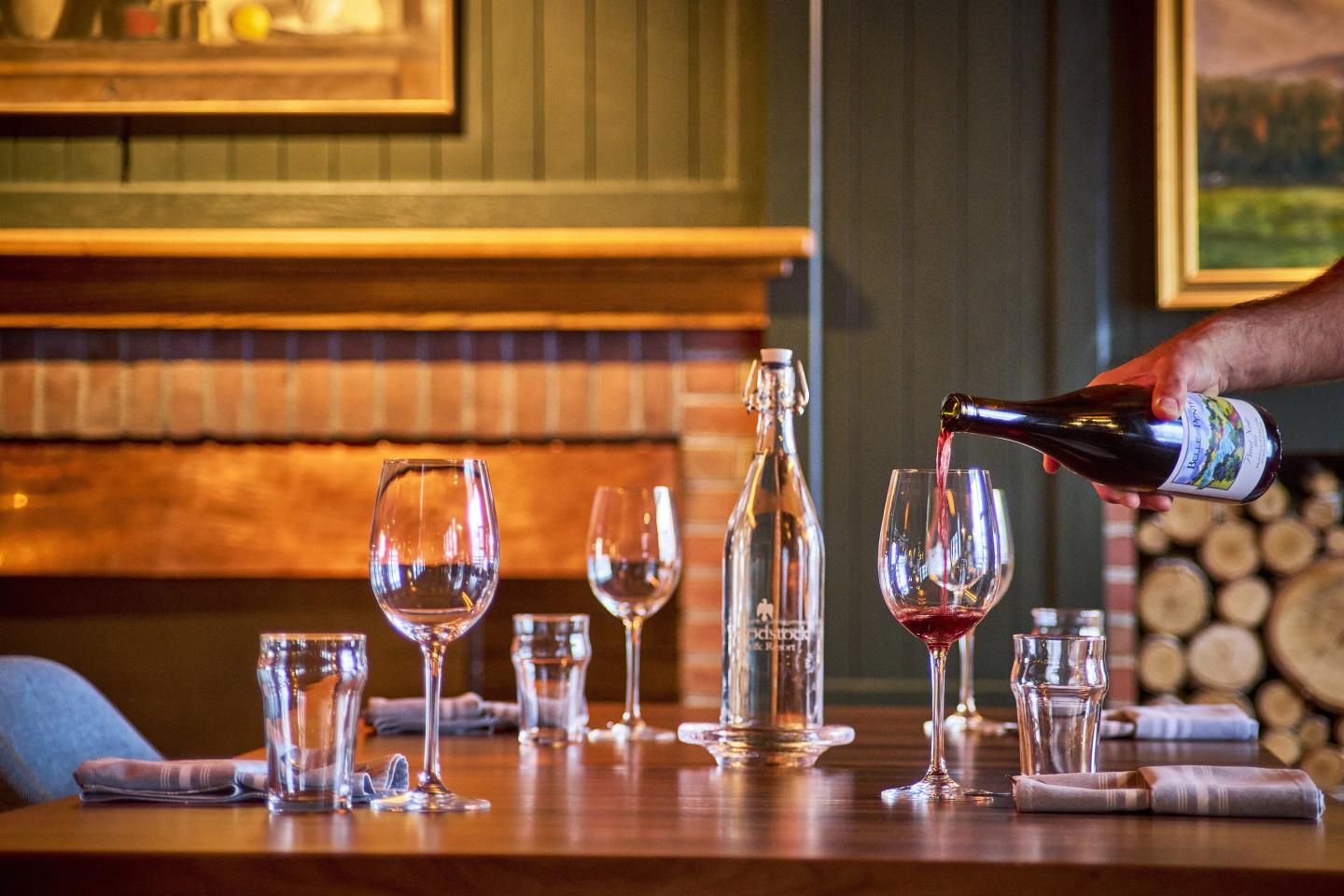 Elegant table setting with wine being poured into glasses. Cozy fireplace in the background.