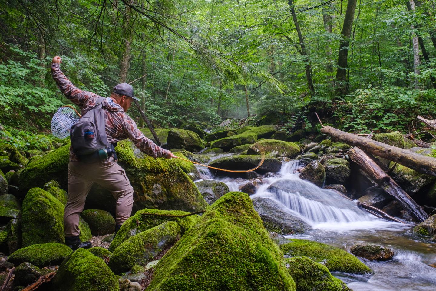 Man fly Fishing over mossy rocks in a forest stream in Vermont.