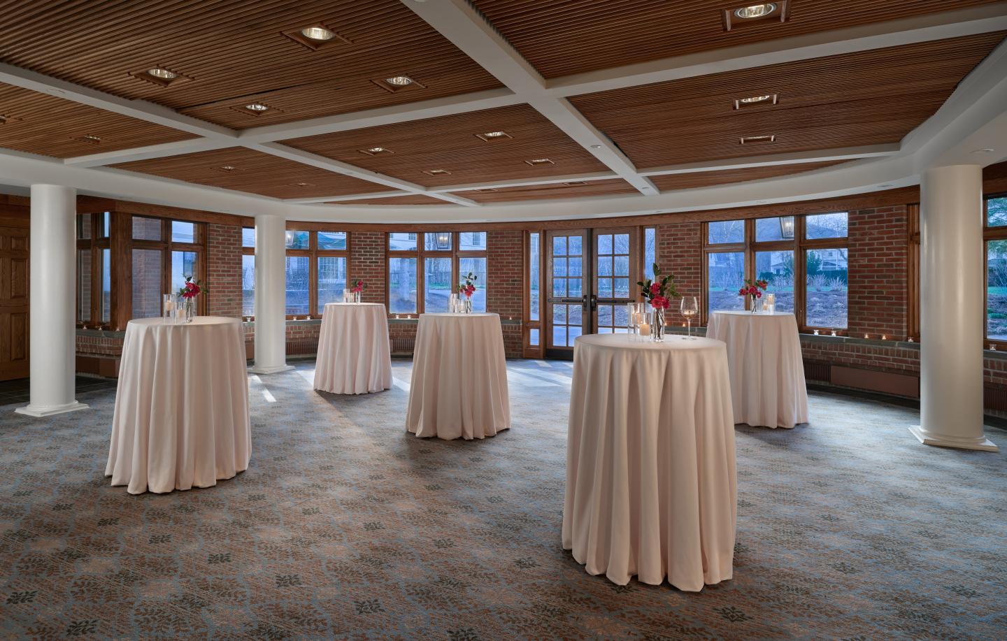 Spacious room with round tables, each with a small floral centerpiece.