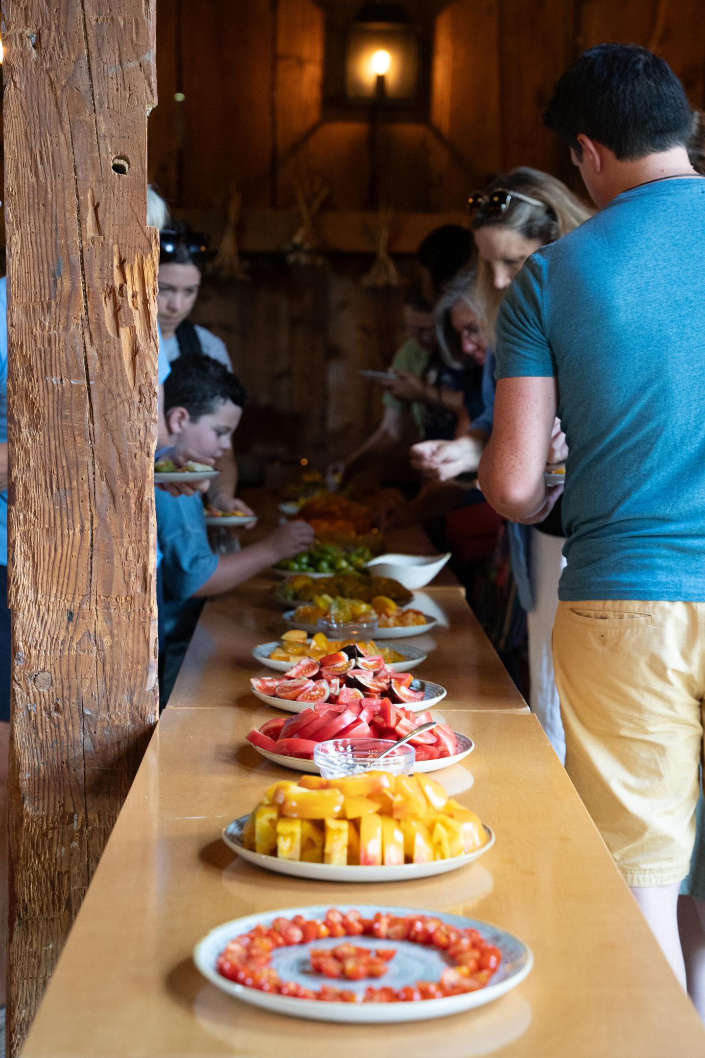 Buffet table with assorted colorful tomatoes. People lining up to serve themselves.