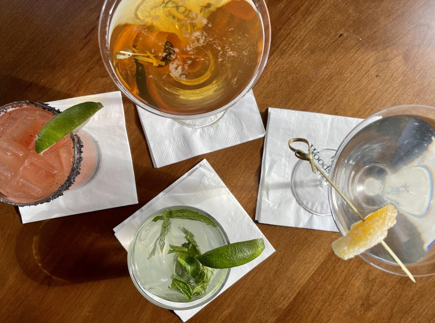 Four cocktails with garnishes on a wooden table.