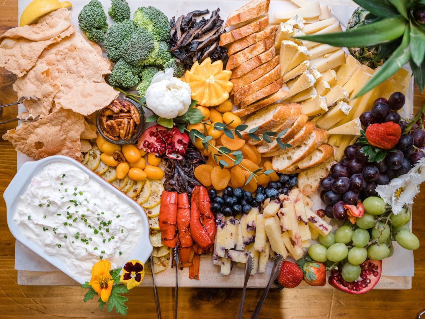 A colorful charcuterie board with fruits, vegetables, cheese, bread, and a dip.