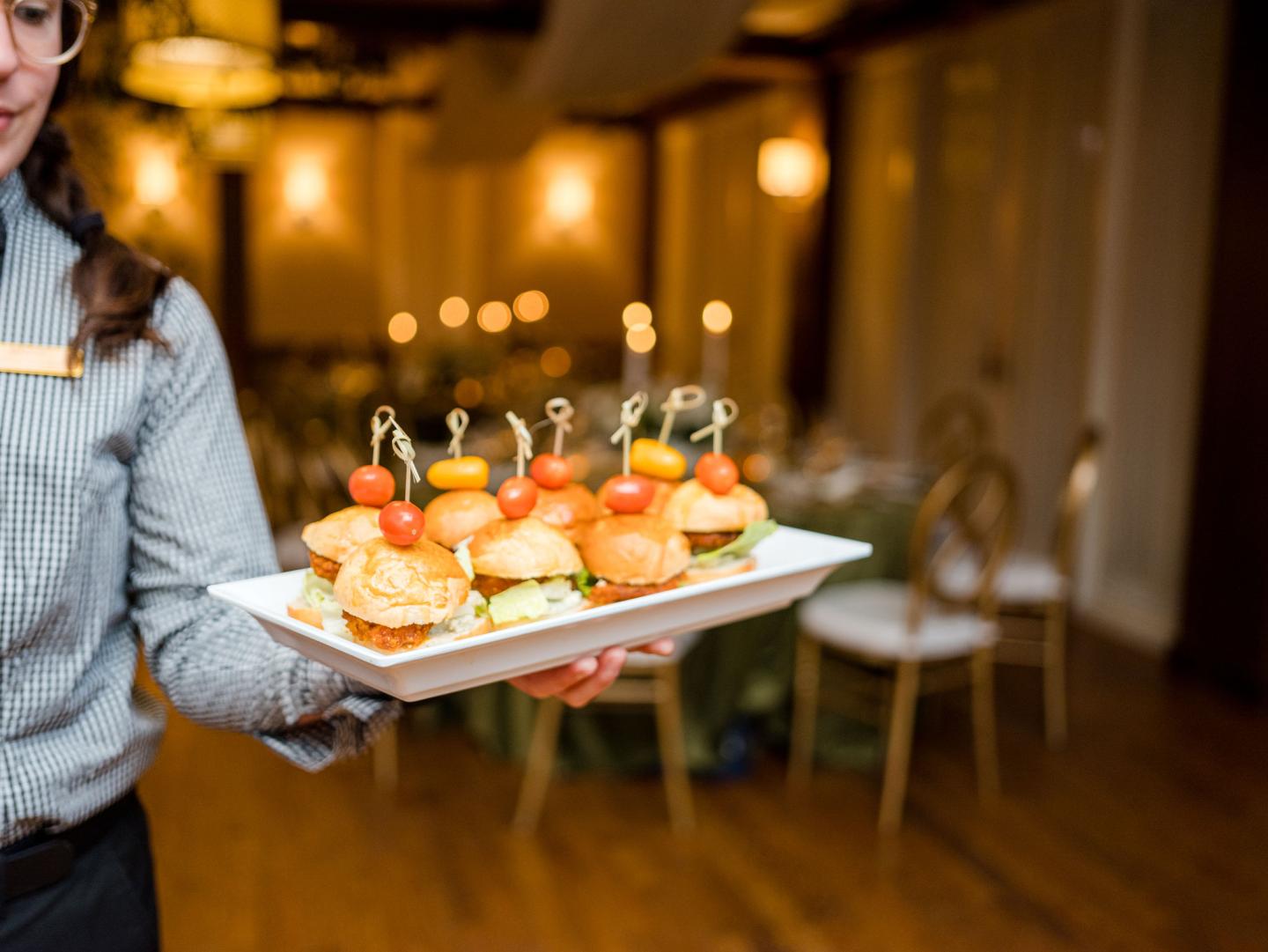 Assorted mini burgers on a platter in an elegant dining room.
