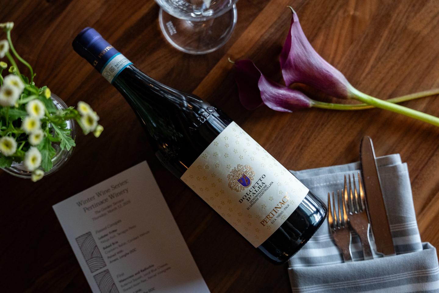 Wine bottle on table with purple flowers, menu, and cutlery.