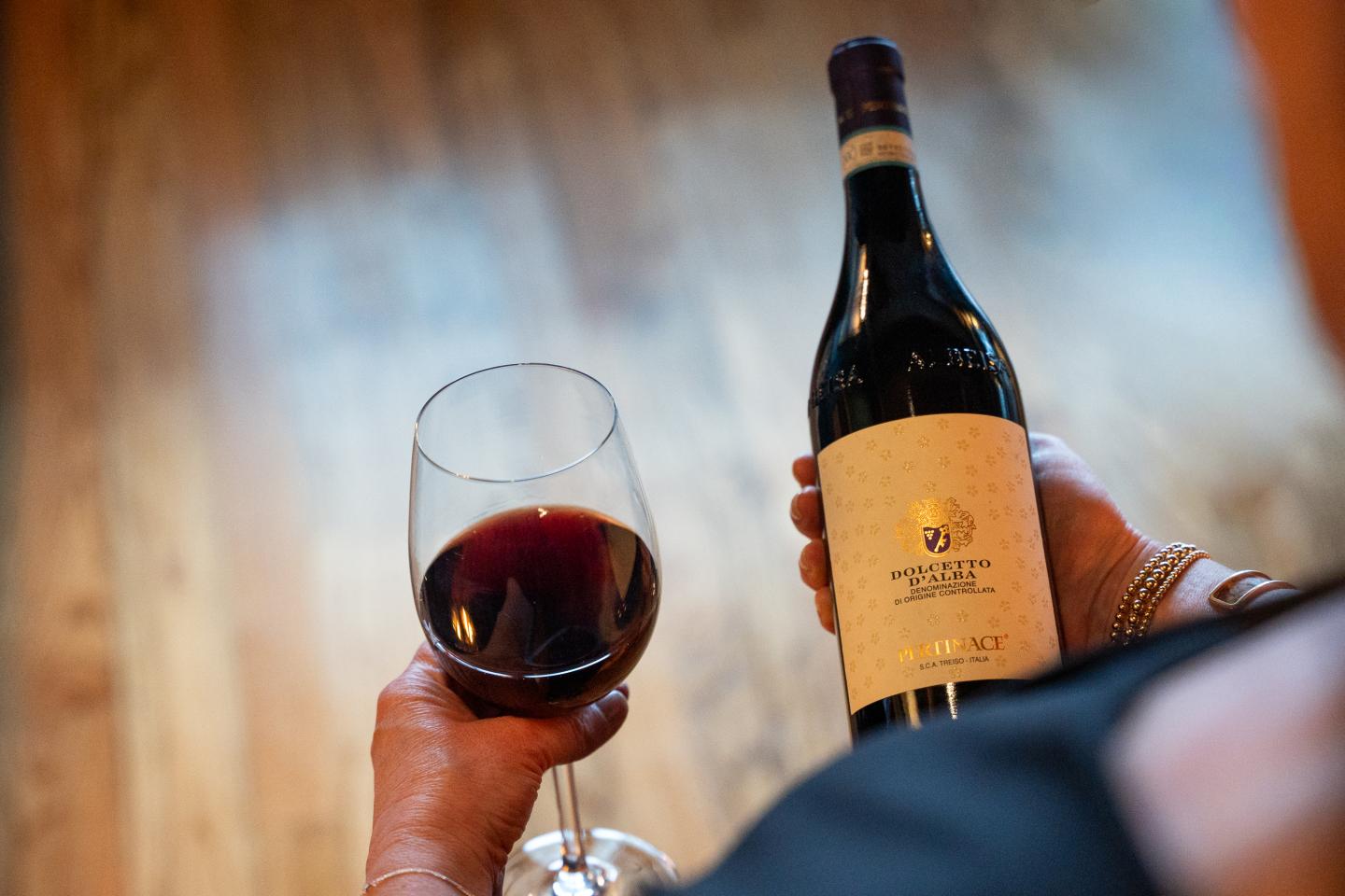 Hand holding a wine bottle and glass on wooden floor background.