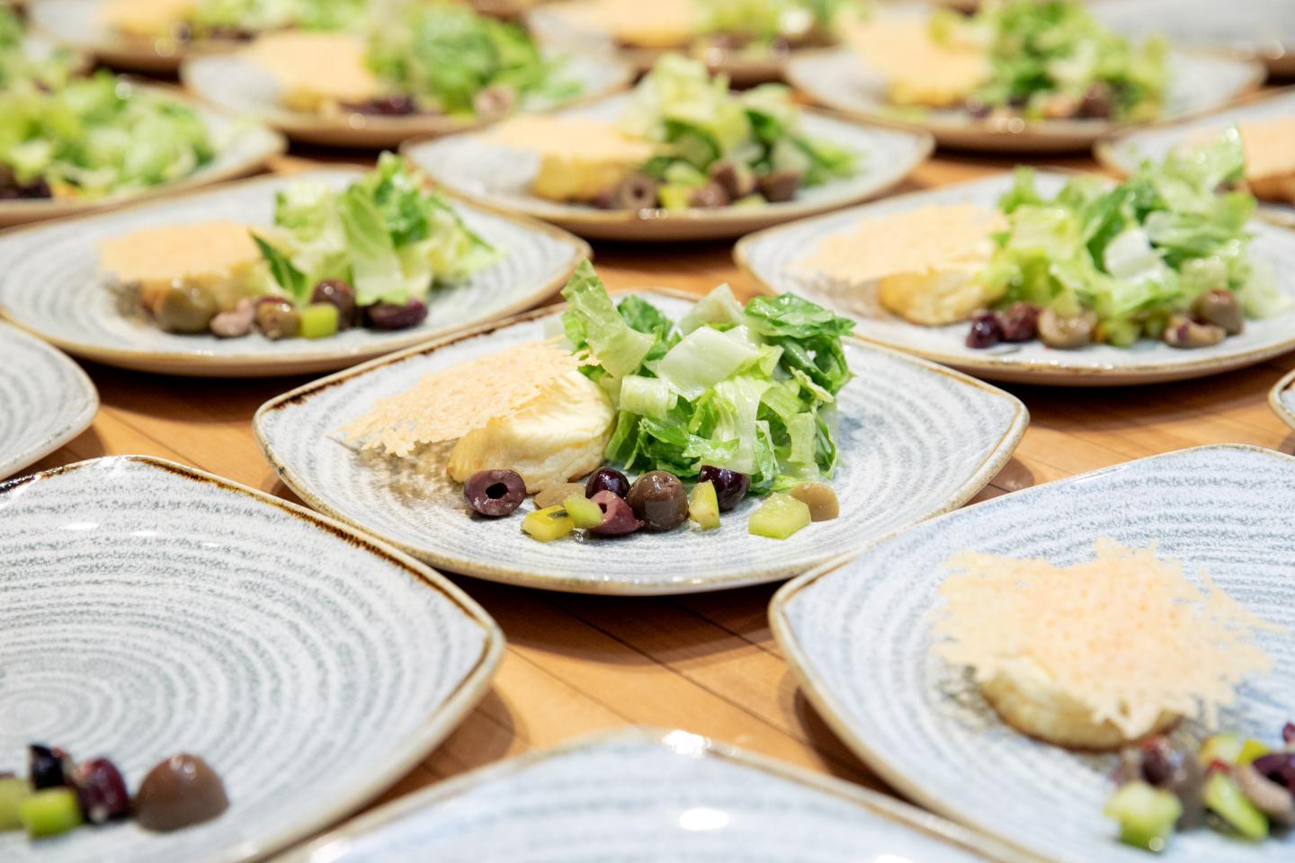Plates of salad with cheese, olives, and greens on a wooden table.