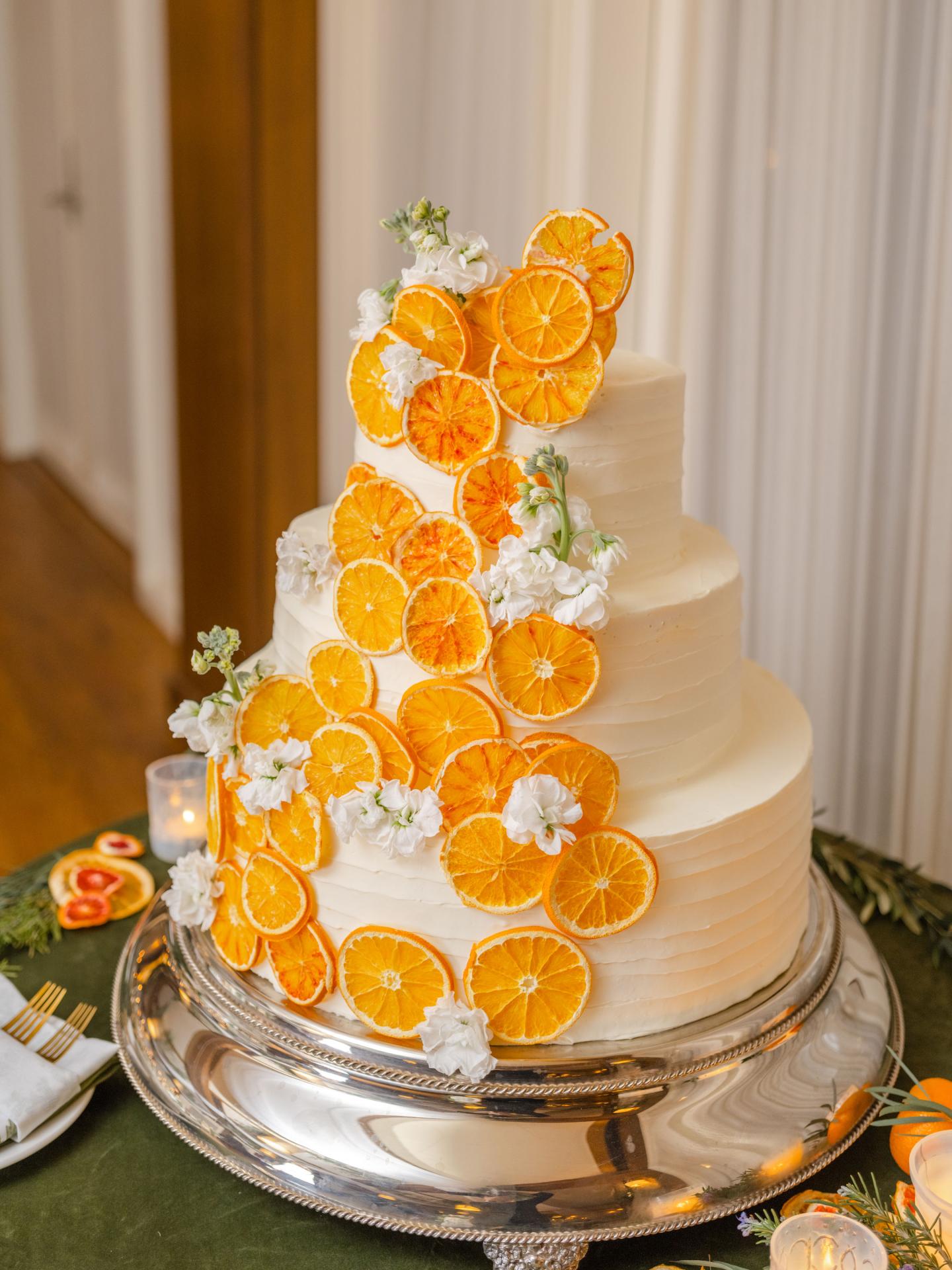 Three-tier white cake with orange slices and white flowers on top.