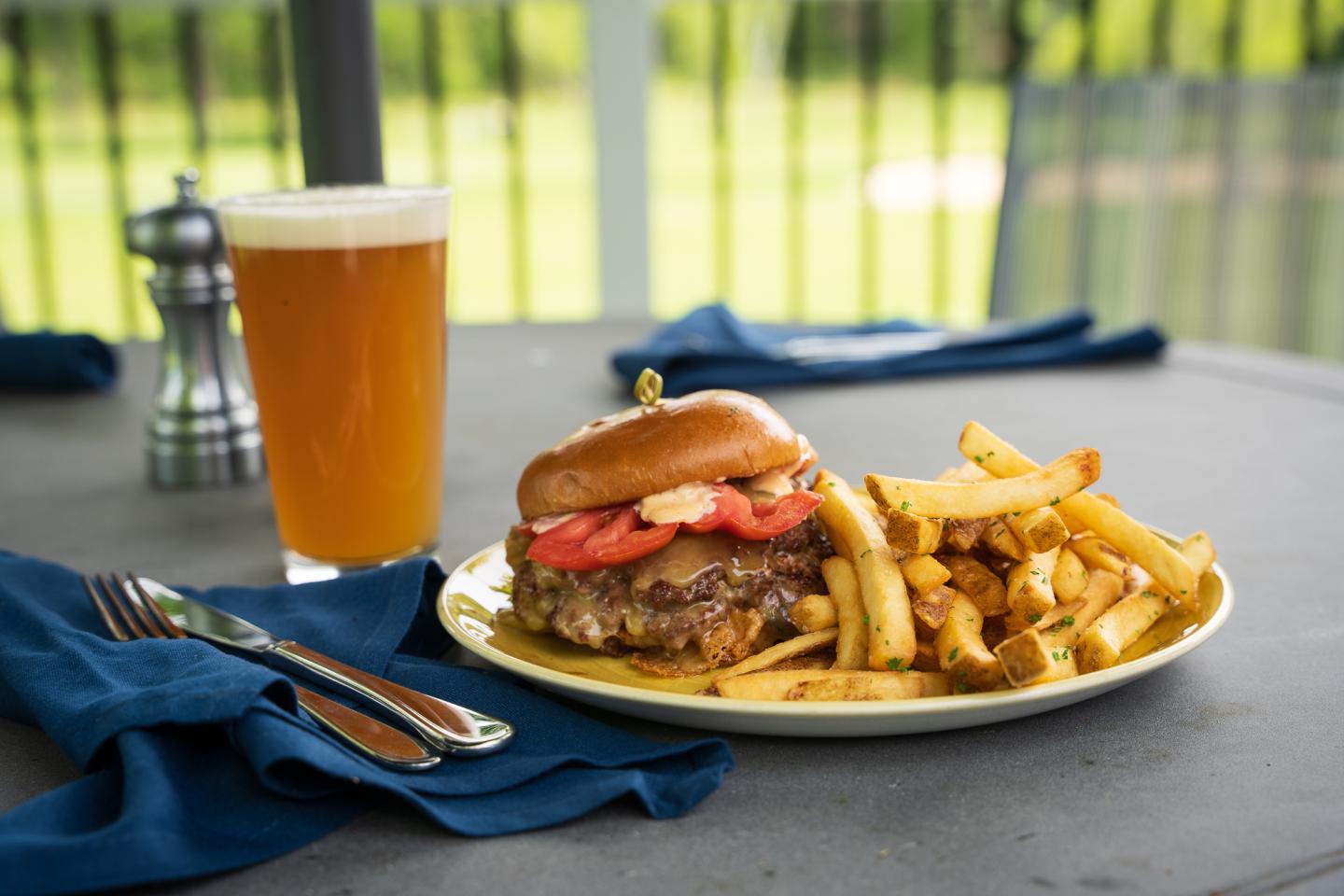 Burger with fries and beer on an outdoor table.
