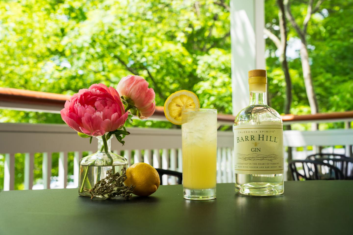 Floral bouquet, cocktail with lemon, and gin on a sunny porch table.