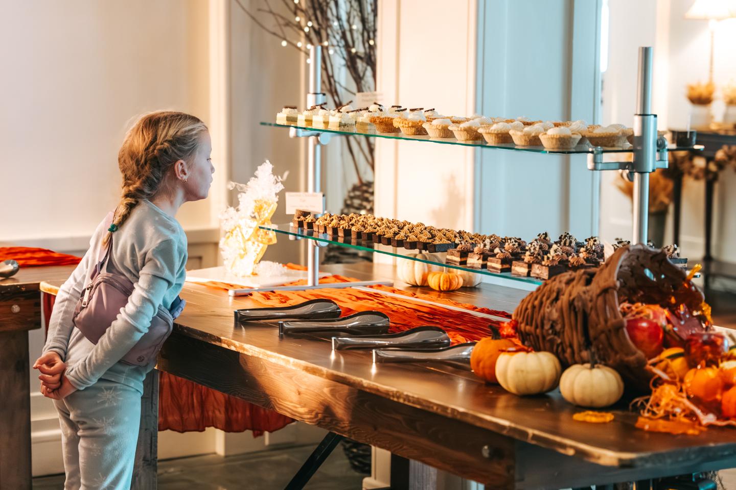 Child admiring a dessert buffet with fall decorations and pumpkins.