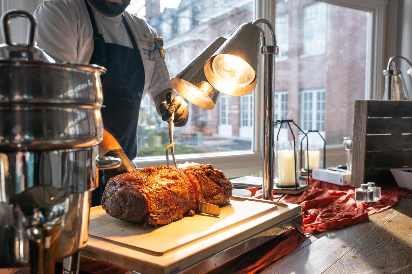 Chef carving herb crusted roast beef under warm lights indoors.