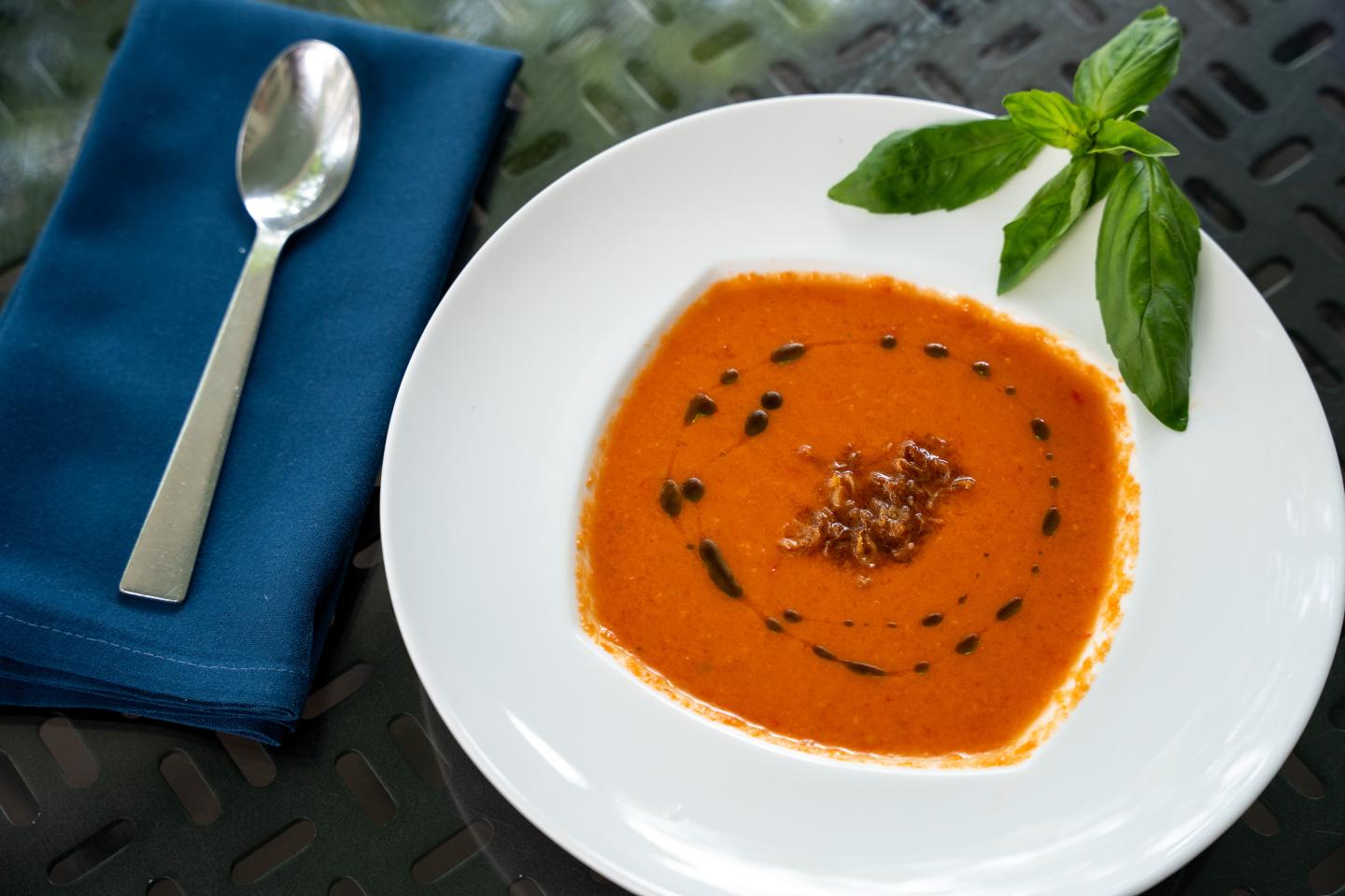 Tomato soup garnished with herbs, next to a spoon on a blue napkin.