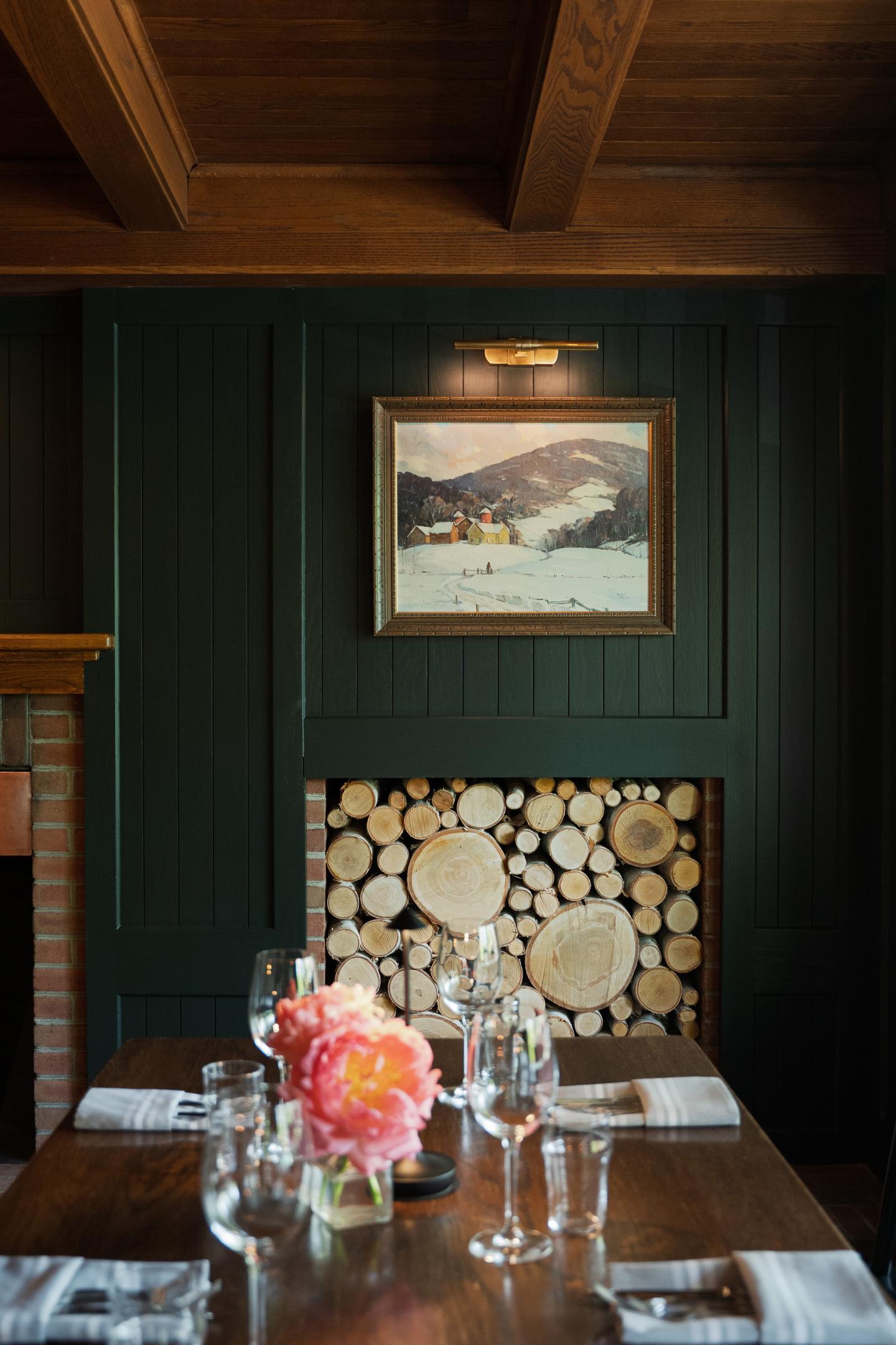 Cozy restaurant setting with wood decor, a table with flowers, and a mountain painting.