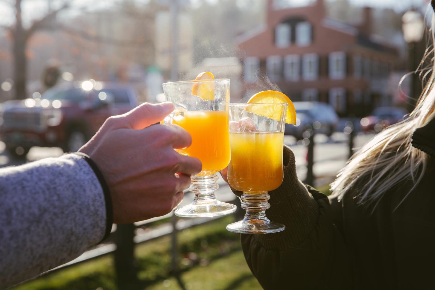 Hands toasting with orange drinks in the sunlight outdoors.